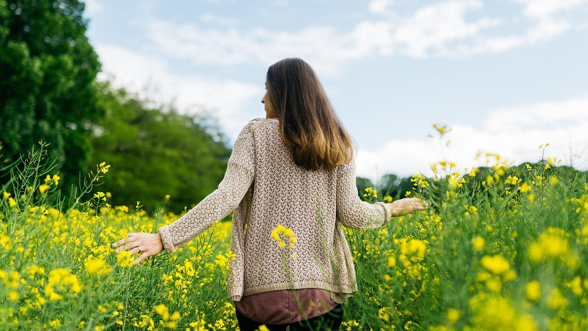 O femeie stă într-un câmp vibrant de flori galbene, bucurându-se de frumusețea naturii din jurul ei