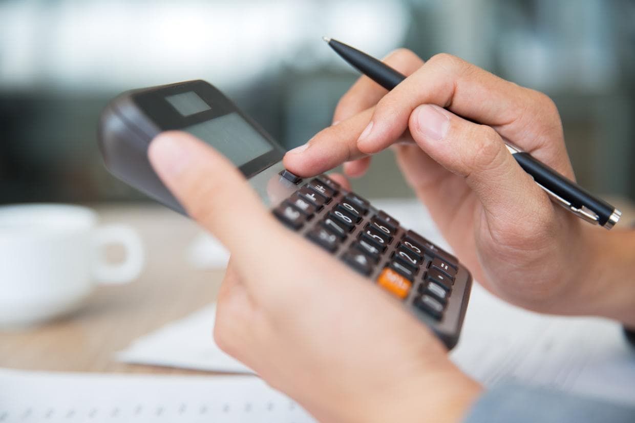 O persoană calculează numere pe un calculator, concentrată asupra sarcinii sale