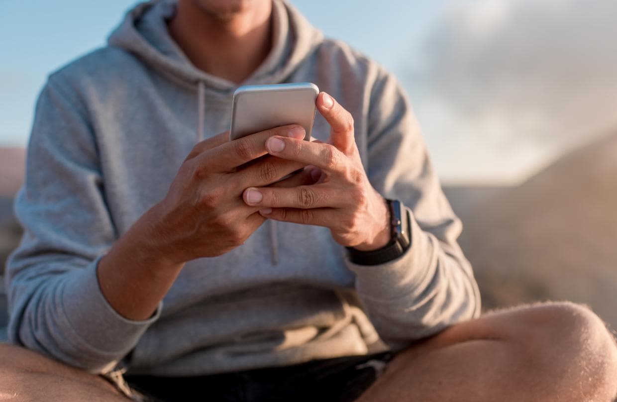 Un bărbat cu hanorac este concentrat folosind smartphone-ul în aer liber