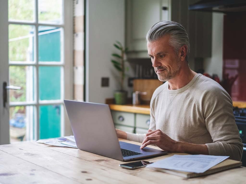 Un bărbat stă pe canapea purtând căști, concentrat asupra telefonului său în timp ce se relaxează